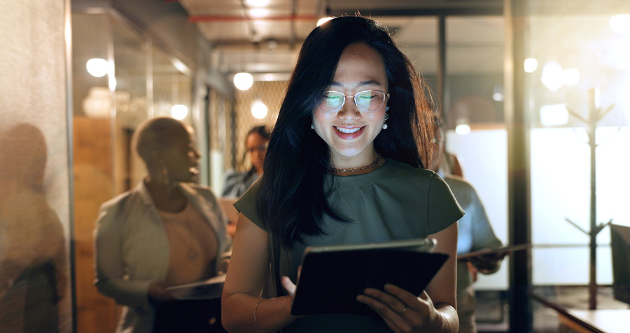 night, tablet and business people walking in office after finishing work task. tech, overtime and asian woman with group of friends going home after working late on sales project in dark workplace.